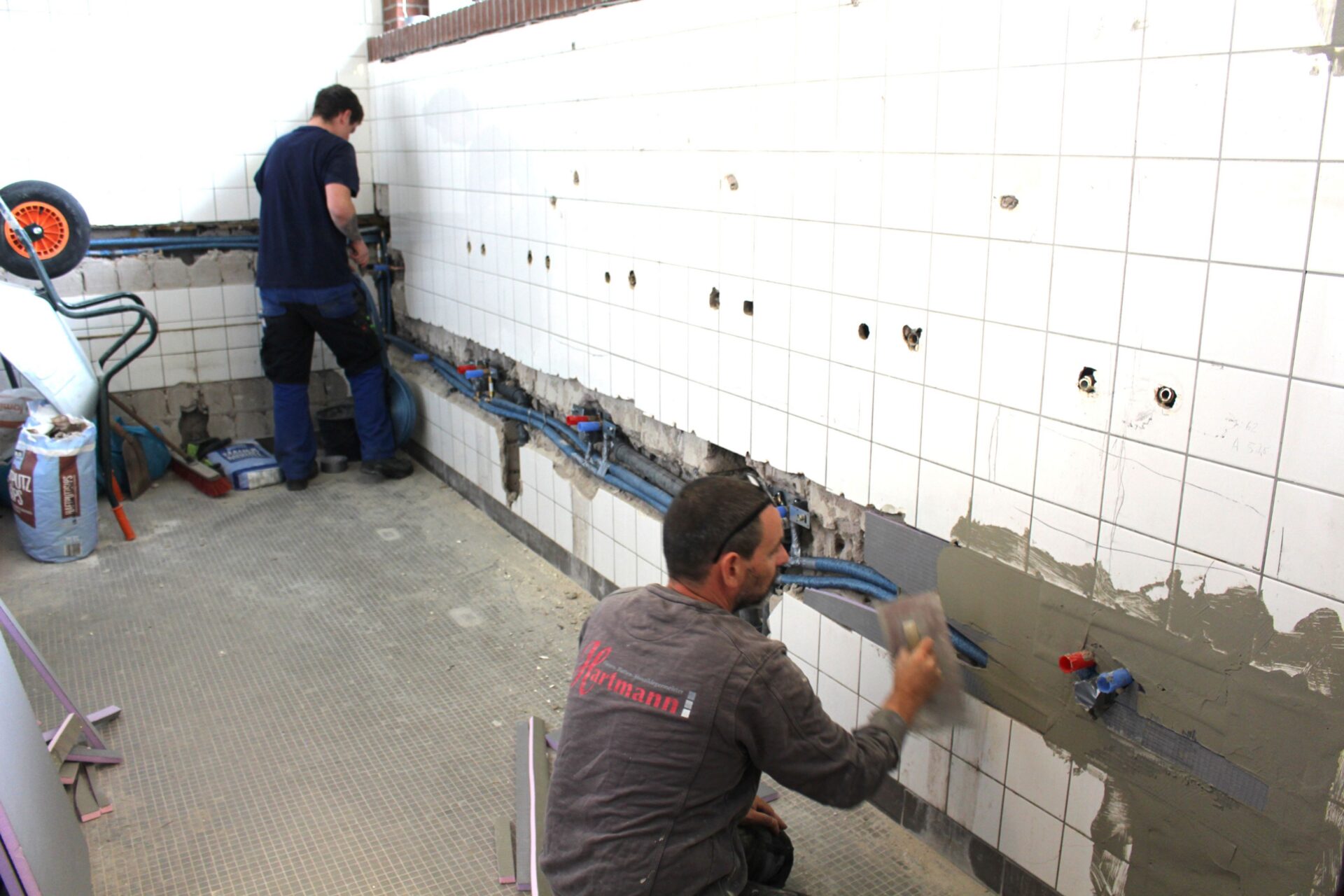 Handwerker bei Fliesen- und Installationsarbeiten im Sanitärbereich der Sporthalle Hemeringen